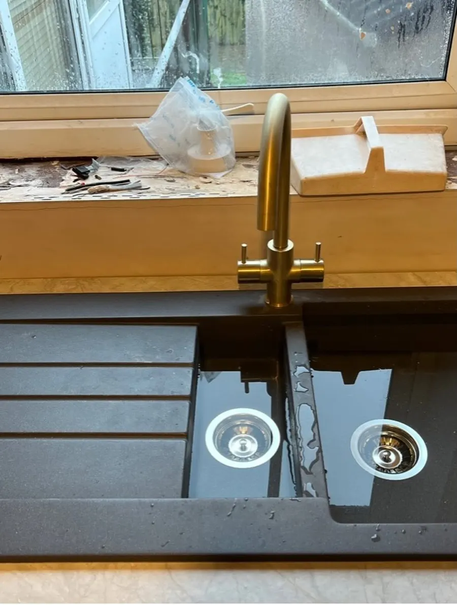 Brushed brass mixer tap over a black composite one and a half bowl kitchen sink