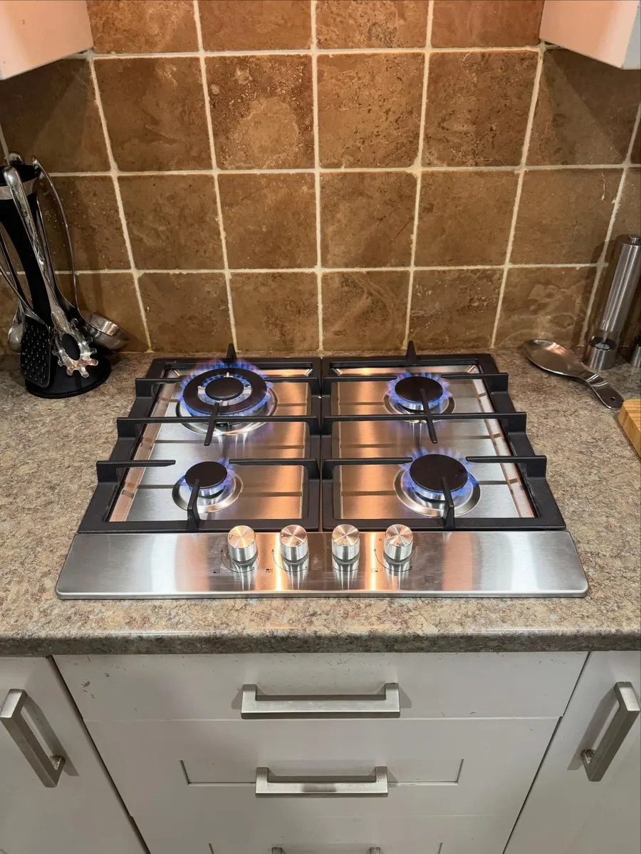 Stainless steel gas hob with all four burners lit in a tiled kitchen