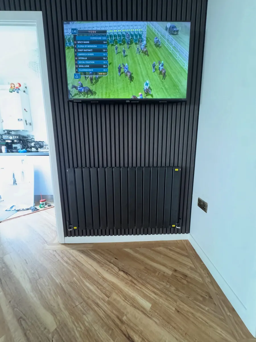 Black panel radiator fitted below a wall-mounted TV on a slatted feature wall