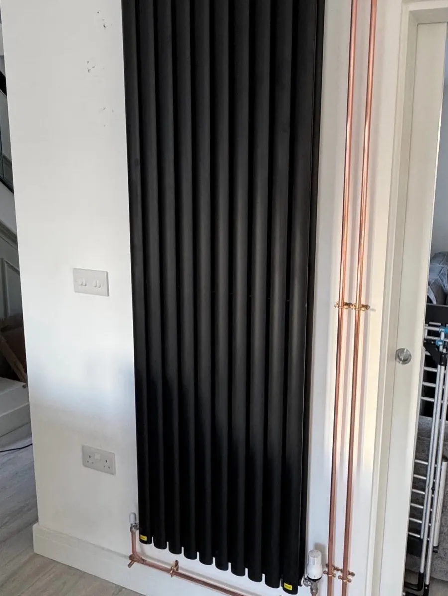 Tall black vertical radiator with exposed copper pipework